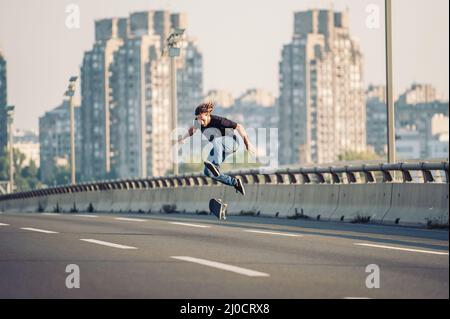 Skater macht Tricks und springt auf der Straßenautobrücke durch den Stadtverkehr. Freies Reiten Skateboard Stockfoto