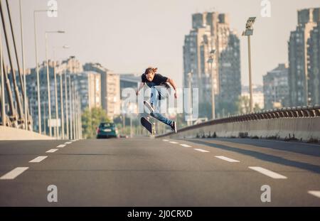 Skater macht Tricks und springt auf der Straßenautobrücke durch den Stadtverkehr. Freies Reiten Skateboard Stockfoto