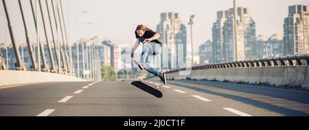 Skater macht Tricks und springt auf der Straßenautobrücke durch den Stadtverkehr. Freies Reiten Skateboard. Panoramaansicht Stockfoto