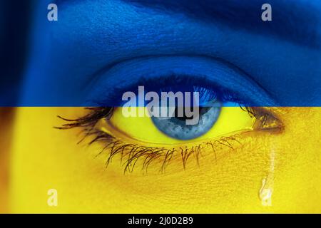 Auge, weinend mit einer Träne, die ihre Wange hinunterlief. Ukraine Flagge über weiblichem Gesicht gemalt Stockfoto