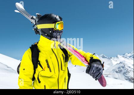 Ein großes Porträt eines Skifahrers in einem Schutzhelm und Brille ist eine Maske und Schal mit Skiern auf der Schulter in der schneebedeckten Stockfoto