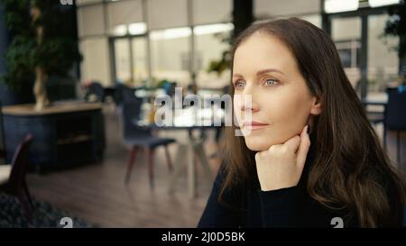 Porträt einer Frau, die im Restaurant sitzt, wartet, denkt, lächelt. Stockfoto