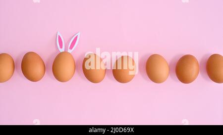 Ostern pastellrosa Hintergrund mit natürlichen Eiern und eine andere mit Hasenohren. Flach legen minimal. Frühlingsferien Stockfoto