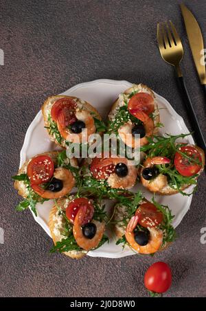 Bruschetta mit Garnelen, Rucola, Frischkäse und Kirschtomaten auf braunem Hintergrund, Draufsicht Stockfoto