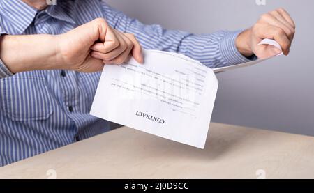 Mann Hände Nahaufnahme brechen Vertrag. Beendigung des Vertrags und des Vertragskonzepts. Mann, der im Büro am Schreibtisch sitzt und ein Dokument zerreißt. Hochwertige Fotos Stockfoto