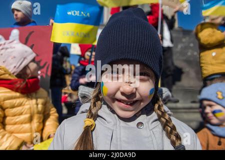 Warschau, Polen. 18. März 2022. Ein ukrainisches Kind lächelt während des Protestes mit ukrainischer Flagge auf ihre Wangen. Der "Marsch der ukrainischen Mütter" fand in Warschau statt, der auch ein Protest gegen den Krieg und die Tötung ukrainischer Kinder war. Die Parolen des marsches waren: "Welt, helft unseren Kindern", "Stoppt den Krieg", "rettet Kinder der Ukraine" und "schließt den Himmel". An dem Protest nahmen vor allem ukrainische Mütter und ihre Kinder Teil, die vor dem Krieg in Polen Zuflucht fanden. Kredit: SOPA Images Limited/Alamy Live Nachrichten Stockfoto