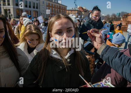 Warschau, Polen. 18. März 2022. Während des Protestes wird eine ukrainische Flagge auf das Gesicht einer Frau gemalt. Der "Marsch der ukrainischen Mütter" fand in Warschau statt, der auch ein Protest gegen den Krieg und die Tötung ukrainischer Kinder war. Die Parolen des marsches waren: "Welt, helft unseren Kindern", "Stoppt den Krieg", "rettet Kinder der Ukraine" und "schließt den Himmel". An dem Protest nahmen vor allem ukrainische Mütter und ihre Kinder Teil, die vor dem Krieg in Polen Zuflucht fanden. (Foto von Attila Husejnow/SOPA Images/Sipa USA) Quelle: SIPA USA/Alamy Live News Stockfoto