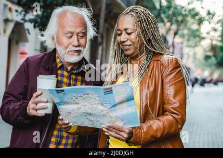 Multirassisches Seniorenpaar auf der Suche nach Wegbeschreibungen auf der Karte im Freien - Ältere Reisende und gesunder Lebensstil - Fokus auf afrikanisches Frauengesicht Stockfoto