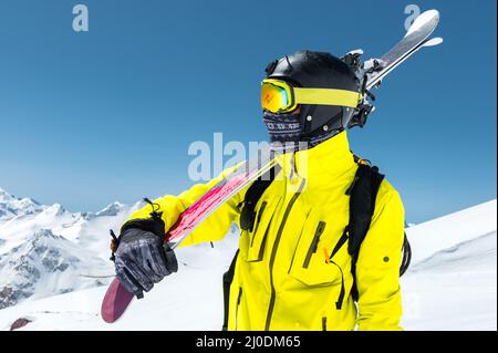 Ein großes Porträt eines Skifahrers in einem Schutzhelm und Brille ist eine Maske und Schal mit Skiern auf der Schulter in der schneebedeckten Stockfoto