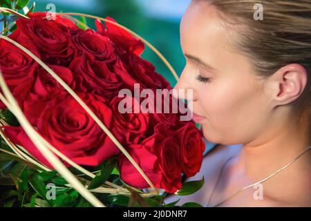 Eine Frau mit einem romantischen Gesicht schnüffelt an der roten Rose Stockfoto