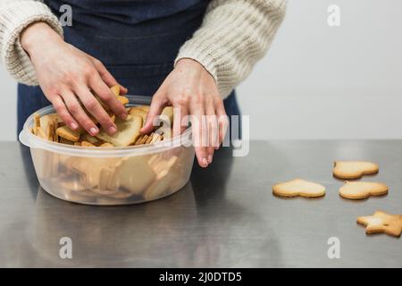 Frau, die frisch gebackene Plätzchen in eine Plastikschüssel legte Stockfoto