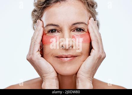 Die Pflege Ihrer Haut wird sie länger jünger halten. Aufnahme einer reifen Frau, die unter den Augen Gelflecken trägt, während sie vor weißem Hintergrund posiert Stockfoto