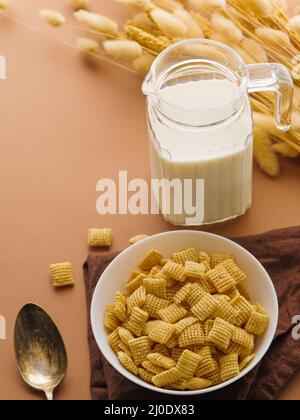 Schnelles Vollkornfrühstück - knusprige Pads in einer Schüssel, Milch in einem Krug und ein paar Cerealien auf beigefarbenem Hintergrund. Es ist ein leeres Leerzeichen zum Einfügen vorhanden. Vi Stockfoto