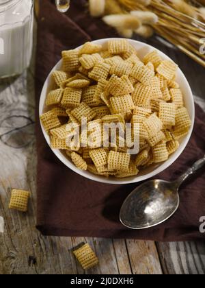 Nahaufnahme. Eine Schüssel mit Vollkornpads und einem Löffel auf einer braunen Serviette. Im Hintergrund ist ein Krug Milch. Schnelles Frühstück, Müsli, gesundes Baby und di Stockfoto