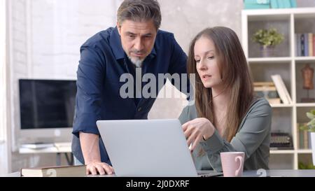 Geschäftsleute, die im Büro mit einem Laptop arbeiten. Glückliches Paar, das von zu Hause an der Rezeption arbeitet. Sprechen, Treffen, Zusammenarbeit, Unternehmer, Berater. Stockfoto