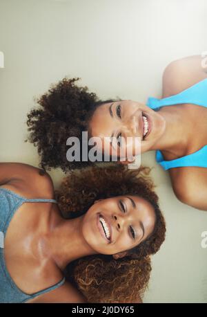 Na ja, das hat Spaß gemacht. Hochwinkelporträt von zwei jungen Frauen, die nach dem Yoga-Kurs auf dem Boden liegen. Stockfoto