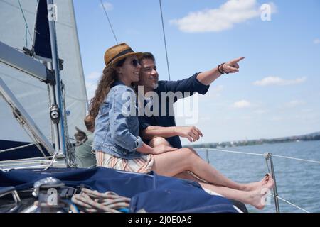 Glückliches lächelndes Paar, das auf einem Segelboot sitzt und Sommer- und Urlaubsreisen genießt. Stockfoto