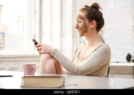 Frau kosmetische Gesichtshaut Pflege. Frau in der Haut Gummi Peeling Gesicht Schönheitsmaske mit Telefon im Home Office. Stockfoto