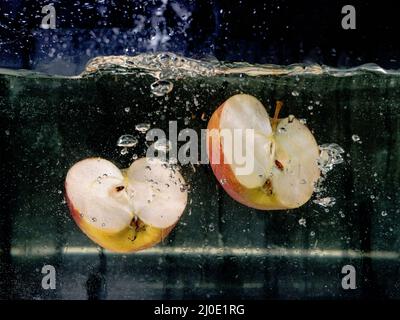 Auf dunklem Grund fallen in Scheiben geschnittene Äpfel ins Wasser. Unterwasseransicht. Kochen, vegetarisch, Kochen zu Hause Konzept Stockfoto