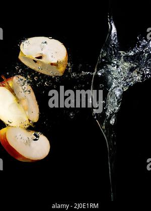 Auf dunklem Grund fallen in Scheiben geschnittene Äpfel ins Wasser. Unterwasseransicht. Kochen, vegetarisch, Kochen zu Hause Konzept Stockfoto