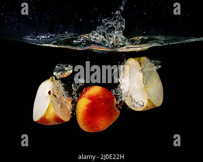 Auf dunklem Grund fallen in Scheiben geschnittene Äpfel ins Wasser. Unterwasseransicht. Kochen, vegetarisch, Kochen zu Hause Konzept Stockfoto