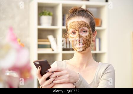 Frau kosmetische Gesichtshaut Pflege. Frau in der Haut Gummi Peeling Gesicht Schönheitsmaske mit Telefon im Home Office. Stockfoto