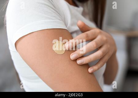 Junge Frau mit aufgetragenen Nikotinpflaster zu Hause, Nahaufnahme. Raucherentwöhnung Stockfoto