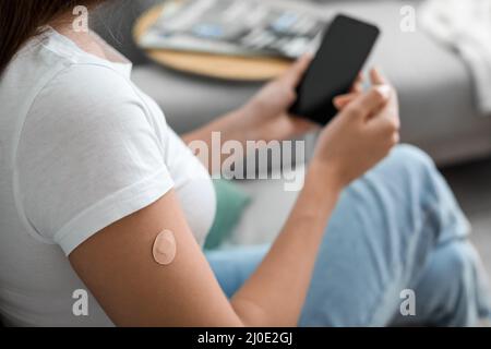 Junge Frau mit aufgetragenen Nikotinpflaster, die zu Hause ein Mobiltelefon verwendet. Raucherentwöhnung Stockfoto