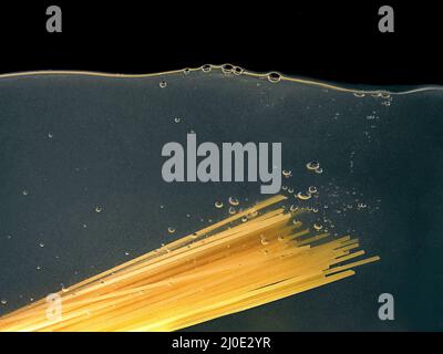 Spaghetti von Hand in einen Topf auf dunklem Hintergrund legen. Unterwasseransicht. Kochen, Kochen zu Hause Stockfoto