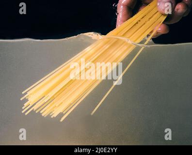 Spaghetti von Hand in einen Topf auf dunklem Hintergrund legen. Unterwasseransicht. Kochen, Kochen zu Hause Stockfoto