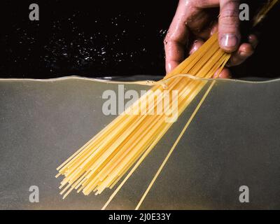 Spaghetti von Hand in einen Topf auf dunklem Hintergrund legen. Unterwasseransicht. Kochen, Kochen zu Hause Stockfoto