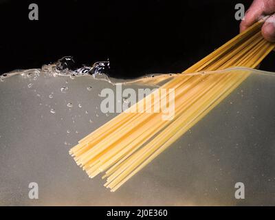 Spaghetti von Hand in einen Topf auf dunklem Hintergrund legen. Unterwasseransicht. Kochen, Kochen zu Hause Stockfoto