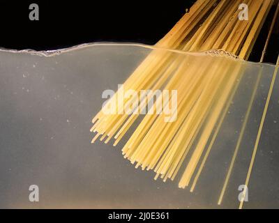 Spaghetti von Hand in einen Topf auf dunklem Hintergrund legen. Unterwasseransicht. Kochen, Kochen zu Hause Stockfoto