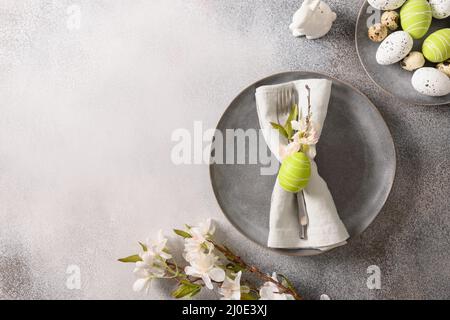 Ostertisch mit grauem Teller, Frühlingsblütenblumen auf grauem Hintergrund. Blick von oben. Platz für Text. Stockfoto