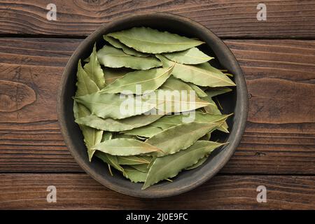 Holzschale aus getrockneten Lorbeerblättern. Grüne Lorbeerblätter auf Holzbrett, Draufsicht. Stockfoto