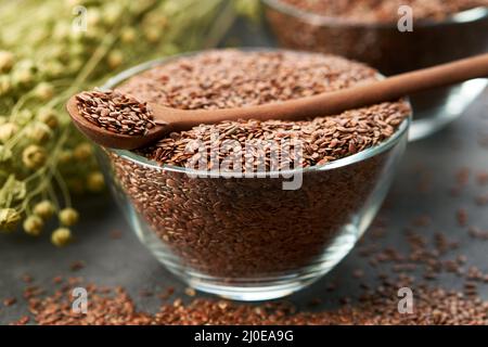 Schüssel mit ganzen Leinsamen. Glasbecher Leinsamen, Leinenbündel auf dem Tisch. Stockfoto