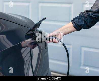 Akkuladegeräte Verbinden Sie sich mit einem Elektroauto. Weibliche Hände, die ein Ladegerät in die Steckdose stecken Stockfoto