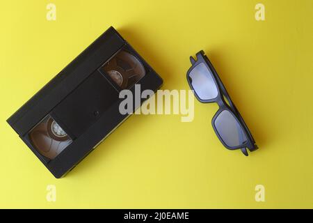 Brille zum Ansehen von 3D Filmen und Videoband auf gelbem Hintergrund, Vintage-Videokassette-Kopierraum Stockfoto