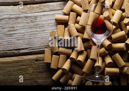 Viele Weinkorken und ein Glas Rotwein auf einem hölzernen Hintergrund. Auf dem Foto befinden sich keine Personen. Restaurant, Hotel, Weinkeller, Weinprobe, gewinnen Stockfoto