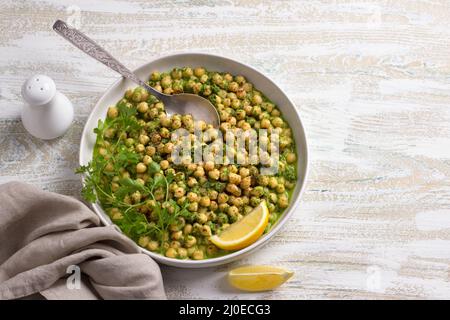Geschmorte Kichererbsen in grüner Sauce mit Petersilie und Zitrone auf weißem Holzhintergrund, rustikaler Stil, Draufsicht. Leckere gesunde hausgemachte Speisen Stockfoto