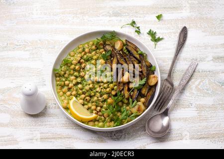 Geschmorte Kichererbsen in grüner Sauce mit gebackener Aubergine, Petersilie und Zitrone auf weißem Holzhintergrund, rustikaler Stil, Draufsicht. Leckeres gesundes Zuhause Stockfoto