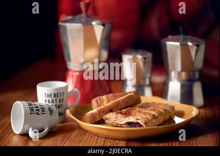 Italienische Kaffeekannen und Gebäck auf einem Tisch mit Tassen Kaffee, Details zu den Tassen und Reflexionen über 3 Größen von Kaffeemaschinen Stockfoto