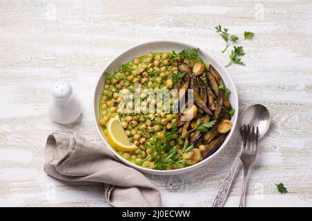 Geschmorte Kichererbsen in grüner Sauce mit Petersilie und Zitrone auf weißem Holzhintergrund, rustikaler Stil, Draufsicht. Leckere gesunde hausgemachte Speisen Stockfoto