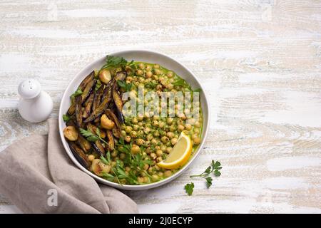 Geschmorte Kichererbsen in grüner Sauce mit gebackener Aubergine, Petersilie und Zitrone auf weißem Holzhintergrund, rustikaler Stil, Draufsicht. Leckeres gesundes Zuhause Stockfoto