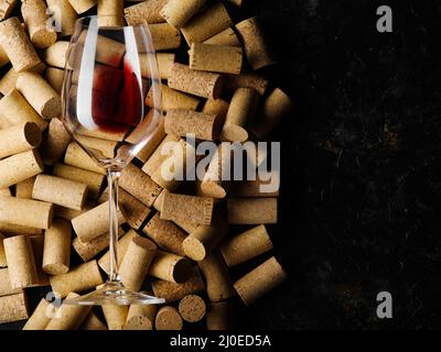 Es gibt viele Weinkorken und ein Glas Rotwein auf schwarzem Hintergrund. Stylische Komposition. Keine Personen. Restaurant, Hotel, Weinkeller. Werbung b Stockfoto