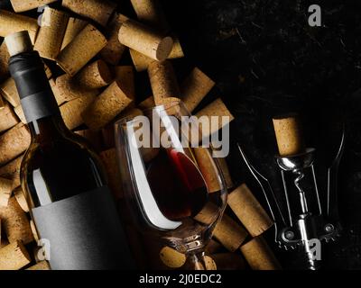 Nahaufnahme. Eine Flasche Rotwein, ein Weinglas, ein Korkenzieher und viele Weinkorken auf schwarzem Hintergrund. Weinsammlung, Weinkeller, Weinprobe, s Stockfoto
