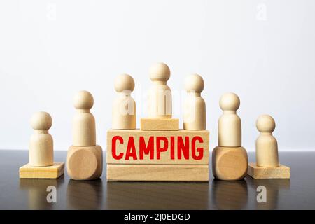 Camping-Wort auf einem Holzwürfelschild mit verschwommenem Hintergrund eines Campingplatzes im Sommer. Stockfoto