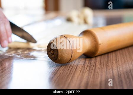 Nahaufnahme eines Nudelnadels auf einem Holztisch mit einer Hand und einem Messer dahinter Stockfoto