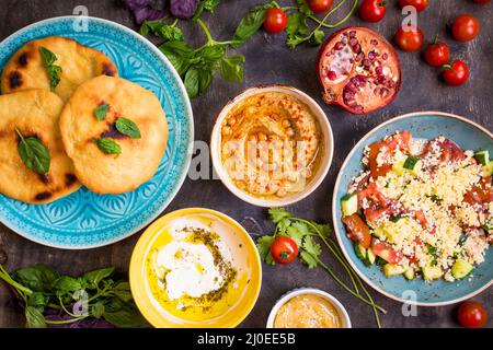 Tisch serviert mit dem Nahen Osten vegetarische Gerichte. Hummus, Tahini, pitta, couscous Salat und Buttermilch Dip mit Olivenöl Stockfoto