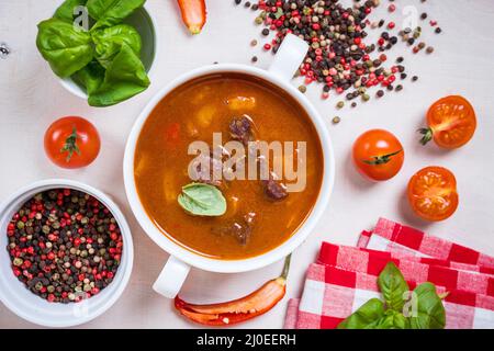 Tomatensuppe mit Fleisch in einer weißen Schüssel auf weißem Holz- Hintergrund Stockfoto